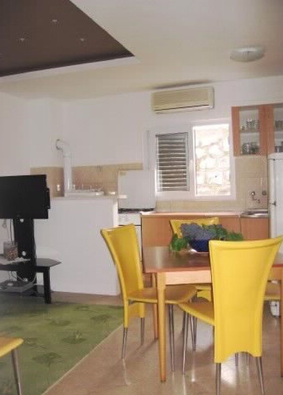 A dining area with yellow chairs, a wooden table, and a television on a stand.