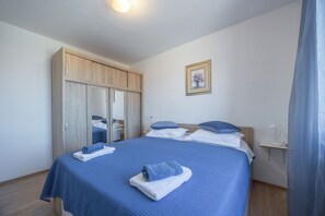 A neatly made bed with blue bedding, a wooden wardrobe, and a small bedside table with a lamp. - Apartment Toma (Supetar)