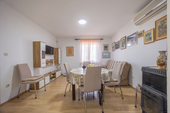 A dining area with a round table, chairs, a television, and framed artwork on the walls. - Apartment Toma (Supetar)