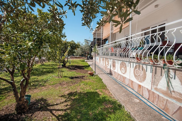 A garden area with a metal fence, potted plants, and a building with a balcony. - Apartment Meri (Trogir)
