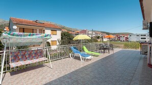 Una terrazza con una panca decorata, due sdraio, un ombrellone giallo e un recinto bianco.