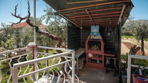 Un'area esterna riparata con un barbecue, un parapetto in metallo bianco e piante in vaso.