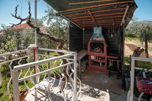 A covered outdoor area with a barbecue grill, a white metal railing, and potted plants. - Apartment Meri (Trogir)