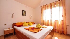 A bedroom with a bed, pillows, a nightstand, a wall-mounted lamp, and a window with curtains.