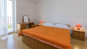 Een slaapkamer met een houten bed, een nachtkastje met een lamp, een dressoir en een raam met gordijnen.