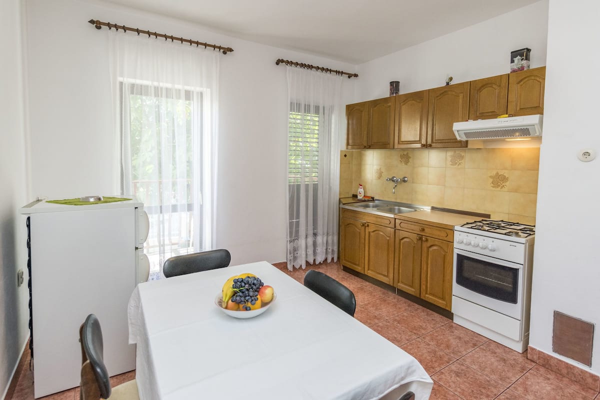 A compact kitchen with a dining table, a refrigerator, wooden cabinets, and a gas stove.