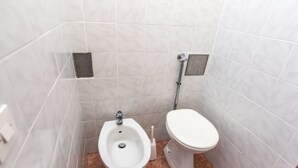 Een kleine betegelde badkamer met een bidet, toilet en een muurbevestigde handdroger.