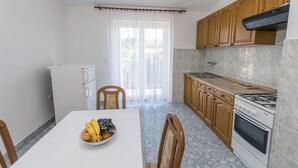 Een kleine keuken met houten kastjes, een witte koelkast, een fornuis en een eettafel met een fruitschaal.