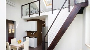 A modern kitchen with white cabinets, a dining table with chairs, and a staircase with a dark wood finish. - Apartments Grzic (Porozina)