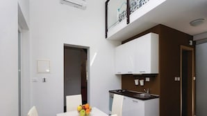 A compact kitchen with white cabinets, a sink, and a dining area with a table and chairs. - Apartments Grzic (Porozina)