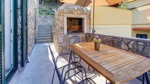 An outdoor patio with a stone fireplace, a wooden table, and chairs. - Apartments Grzic (Porozina)