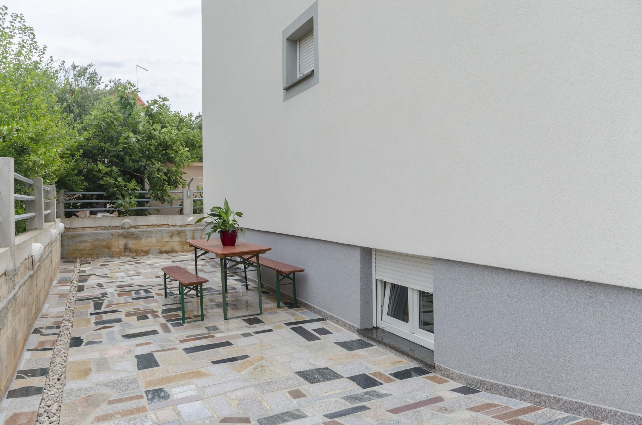 A patio with a tiled floor, a wooden table, a bench, and a potted plant.