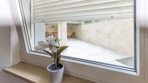 Una ventana con una planta en maceta, vistas de un suelo de baldosas y una barandilla blanca.