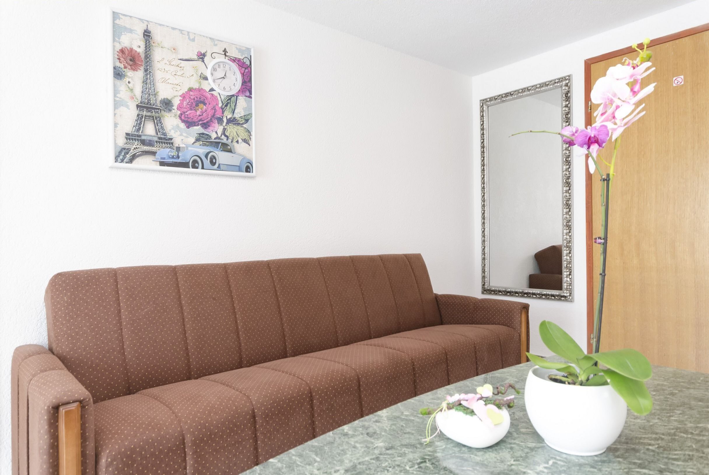 En brun sofa, et marmortæppe, en potteplante, et spejl og en væg med et dekorativt maleri.