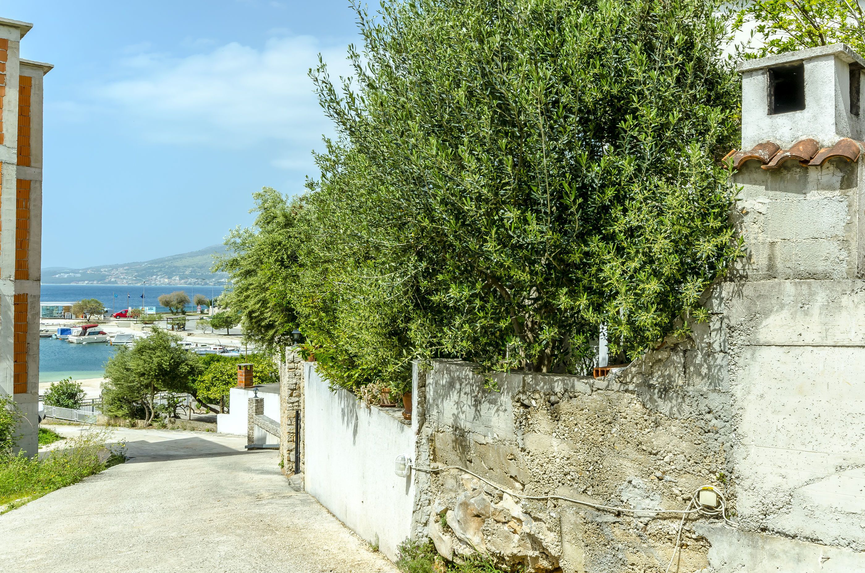 Une route côtière bordée d’un mur de pierres, avec une vue sur la mer et une chaîne de montagnes à l’horizon.