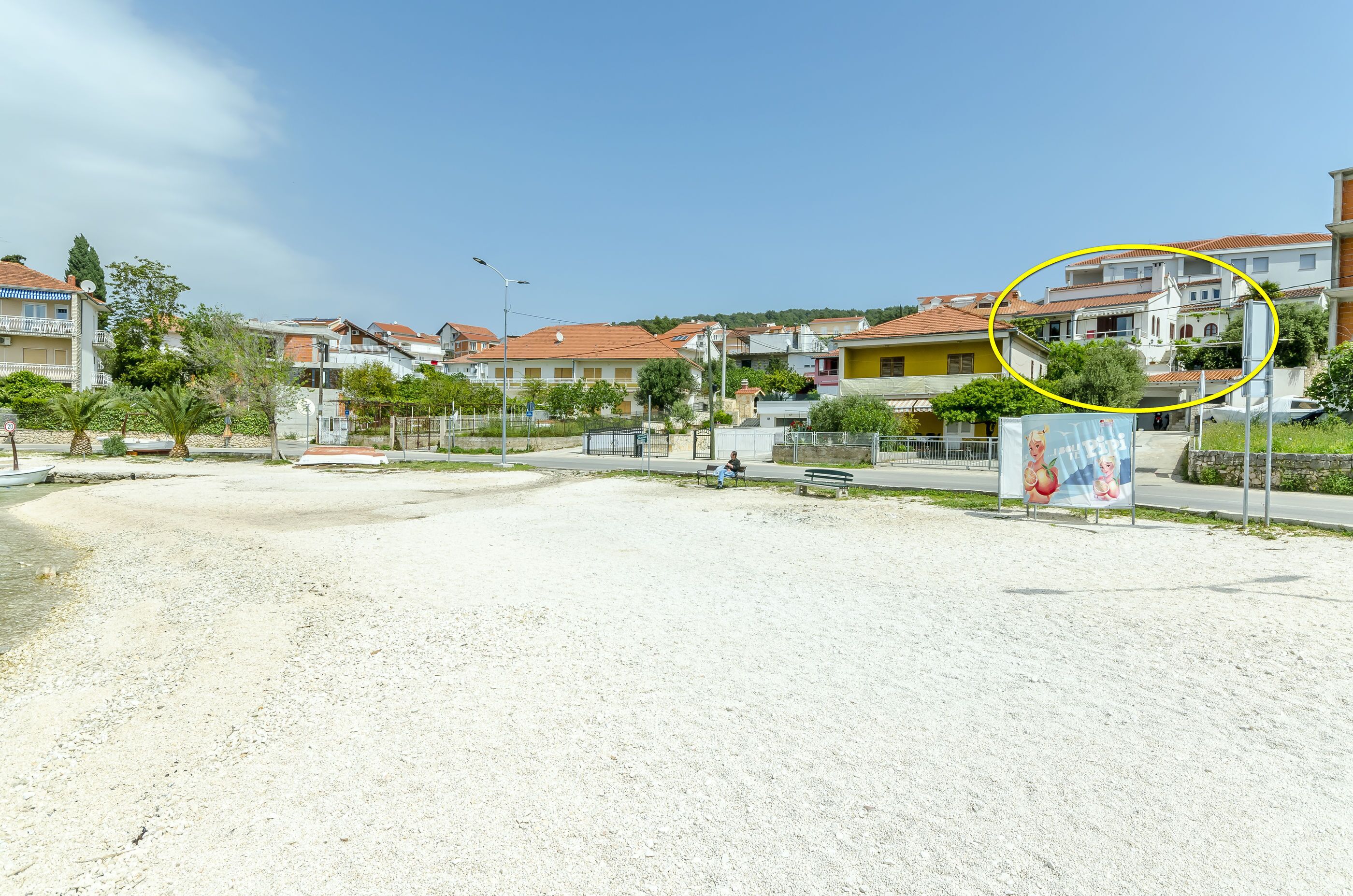 A residential area with houses, a sandy ground, and a billboard.