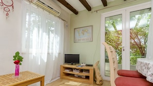 Une pièce avec une table en bois, un téléviseur posé sur un meuble en bois, une chaise rouge et une grande fenêtre donnant sur des arbres.