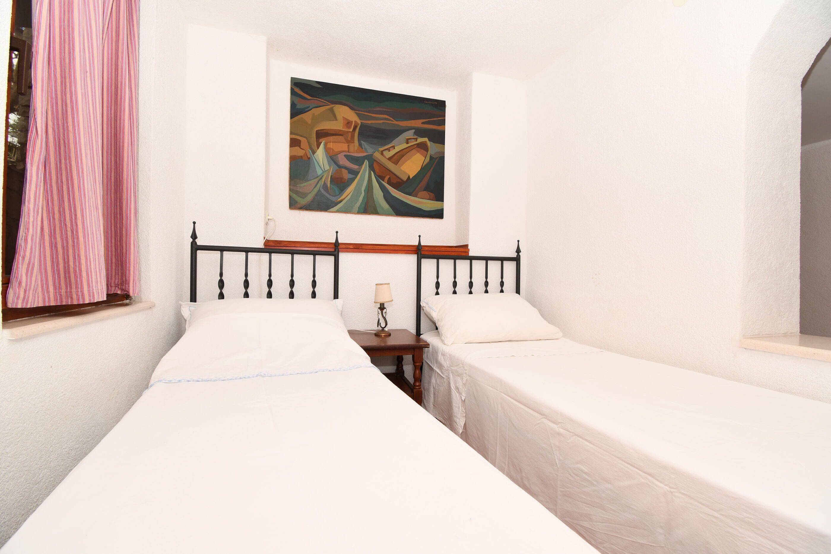 A room with two single beds, a painting on the wall, and a window with pink curtains.