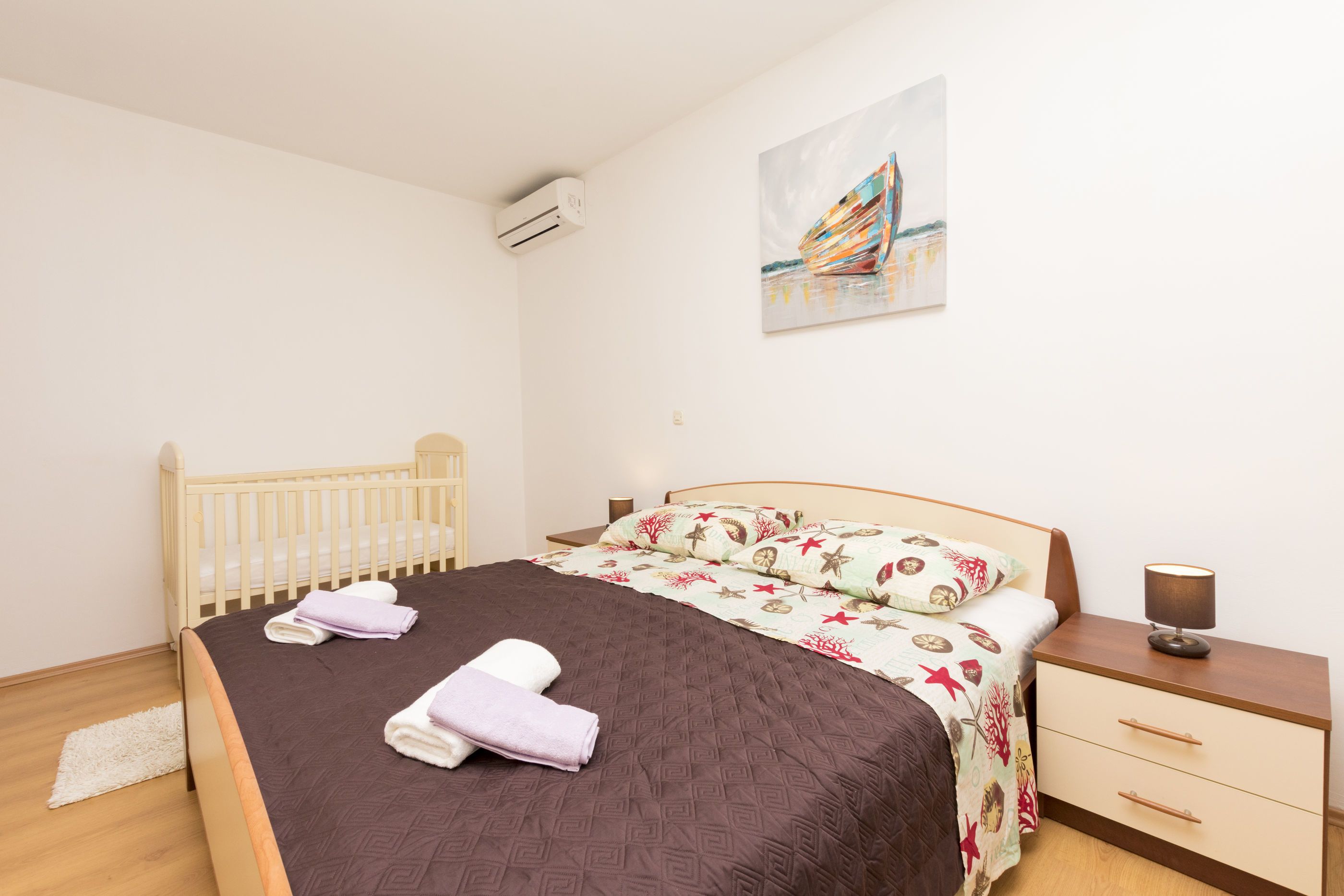 Ein Schlafzimmer mit einem Bett, einem Babybett, einem Nachttisch und einer Wand-Klimaanlage.