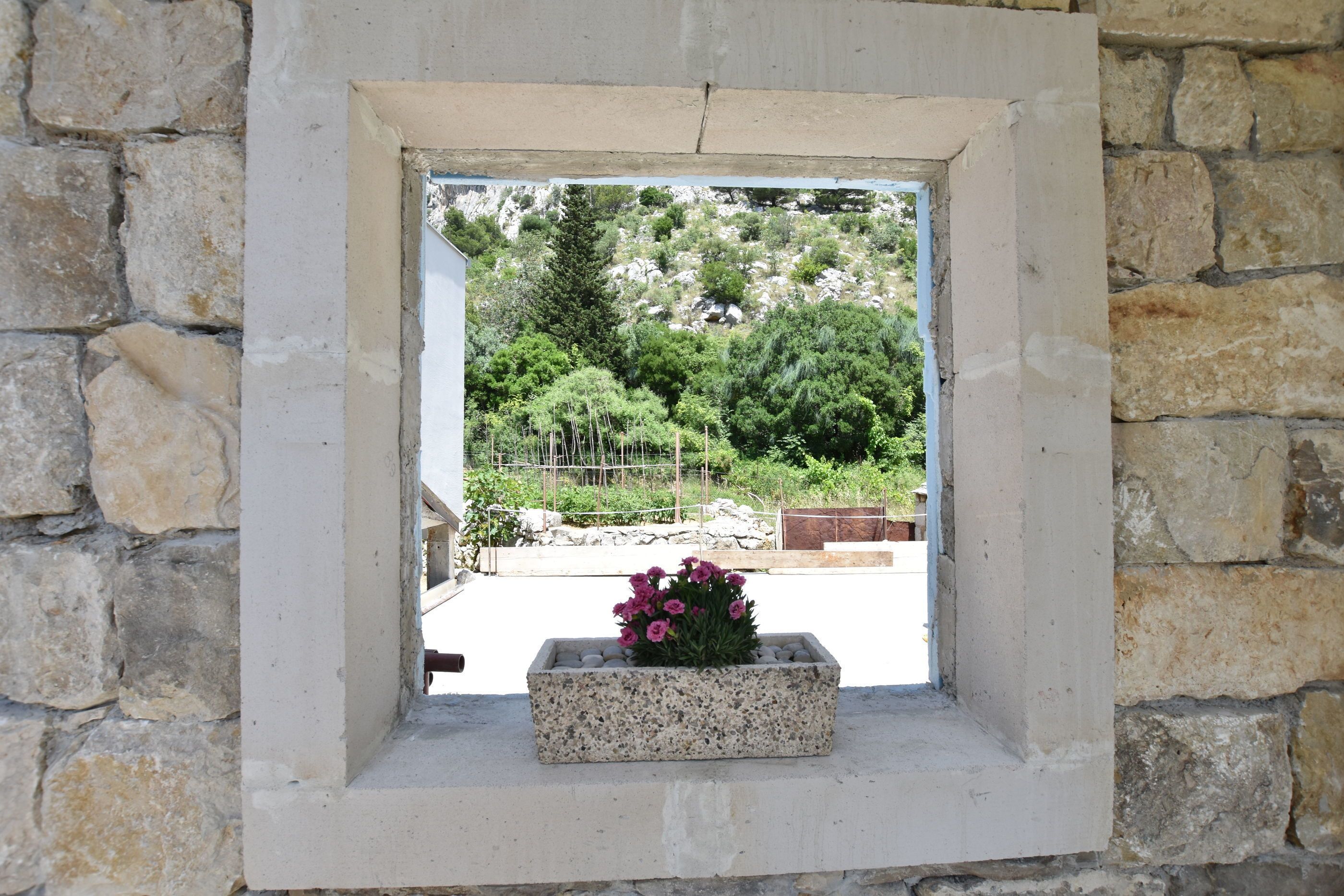 A stone-framed window with a rectangular planter containing pink flowers.