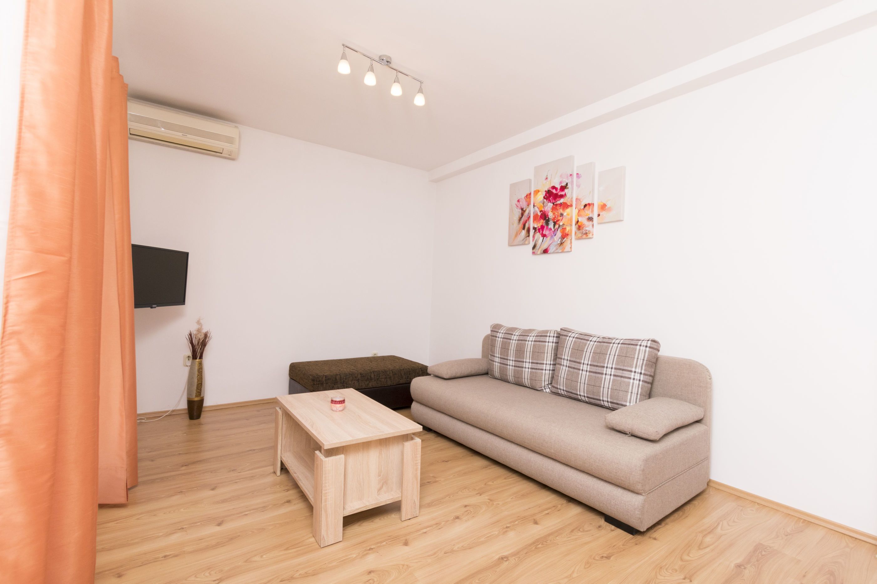A living room with a sofa, a small wooden table, a flat-screen TV, and artwork on the wall.