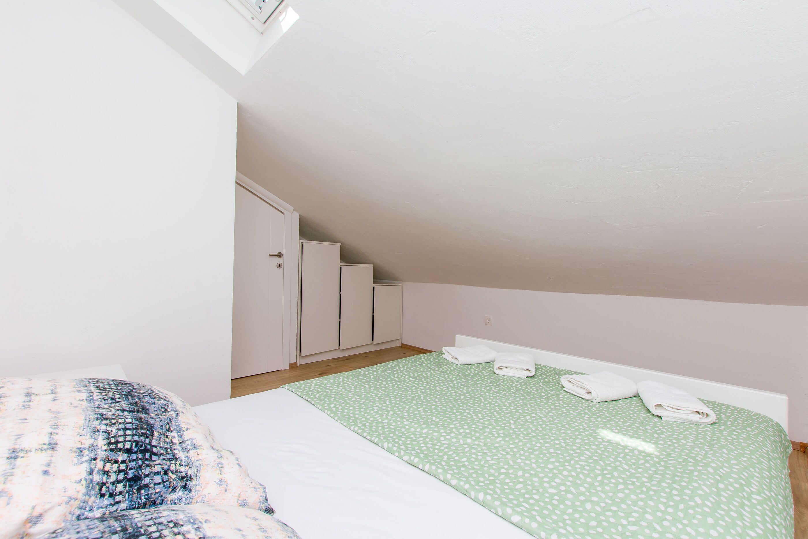 A bedroom with a bed, a green patterned bedspread, and a white door.