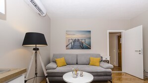 A living room with a grey sofa, two yellow cushions, a white coffee table with decorative items, a floor lamp, and a painting of a pier. - Apartments Cozy Apartments (Vodice)