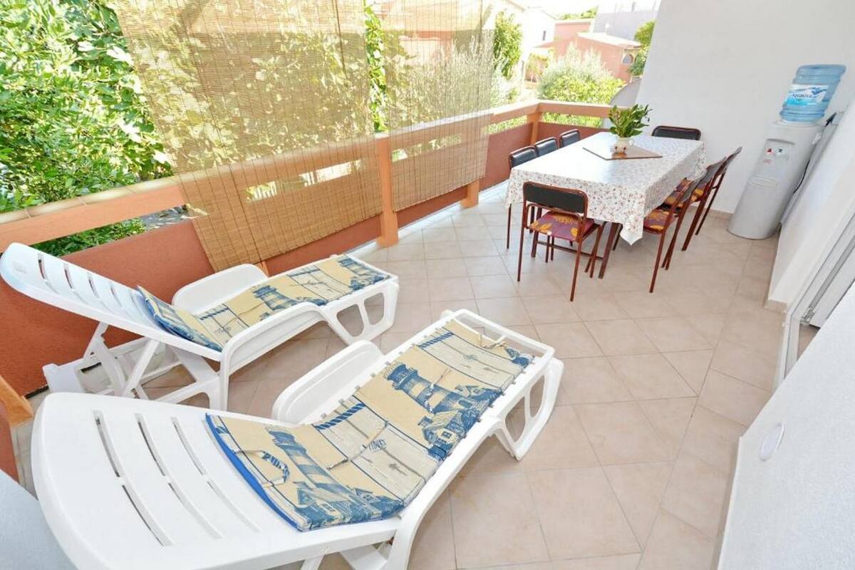 A balcony with white lounge chairs, a table, and chairs.