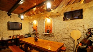 Ein rustikaler Essbereich mit Holztisch und Bänken, Steinwänden und einem an der Wand befestigten Fernseher.
