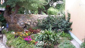 Ein Garten mit einer Steinmauer, verschiedenen blühenden Pflanzen und einem Baum.