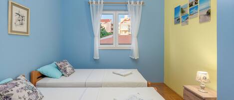 Una habitación con dos camas, una ventana con cortinas, una pared con cuadros y una mesita de noche con una lámpara.