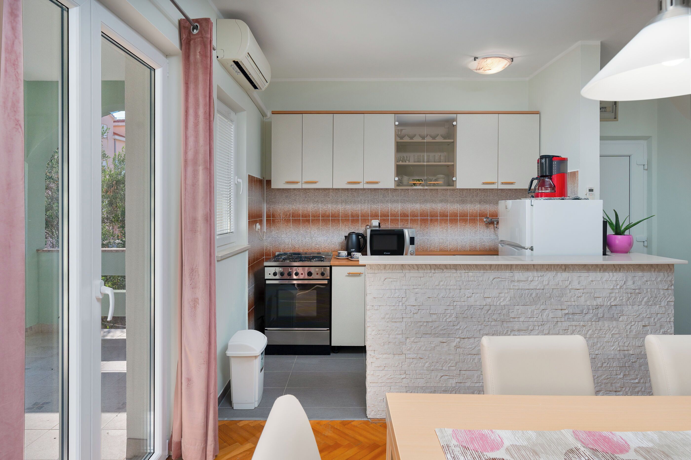 A compact kitchen with white cabinets, a built-in microwave, a coffee maker, and a small island with a sink.