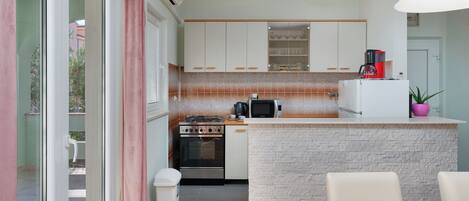 A compact kitchen with white cabinets, a built-in microwave, a coffee maker, and a small island with a sink.