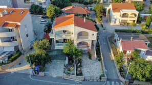 An aerial view of a residential area with stone-paved streets, a central building with a red-tiled roof, and surrounding houses with similar architectural styles. - Apartments Jasna (Novalja)
