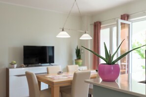 A modern dining area with a wooden table and chairs, a pink potted plant, and a flat-screen TV on a white cabinet. - Apartments Jasna (Novalja)