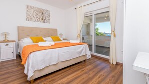 A bedroom with a bed, a nightstand, a lamp, a window with curtains, and a view of the outdoors. - Apartments Jerkunica (Rogoznica)