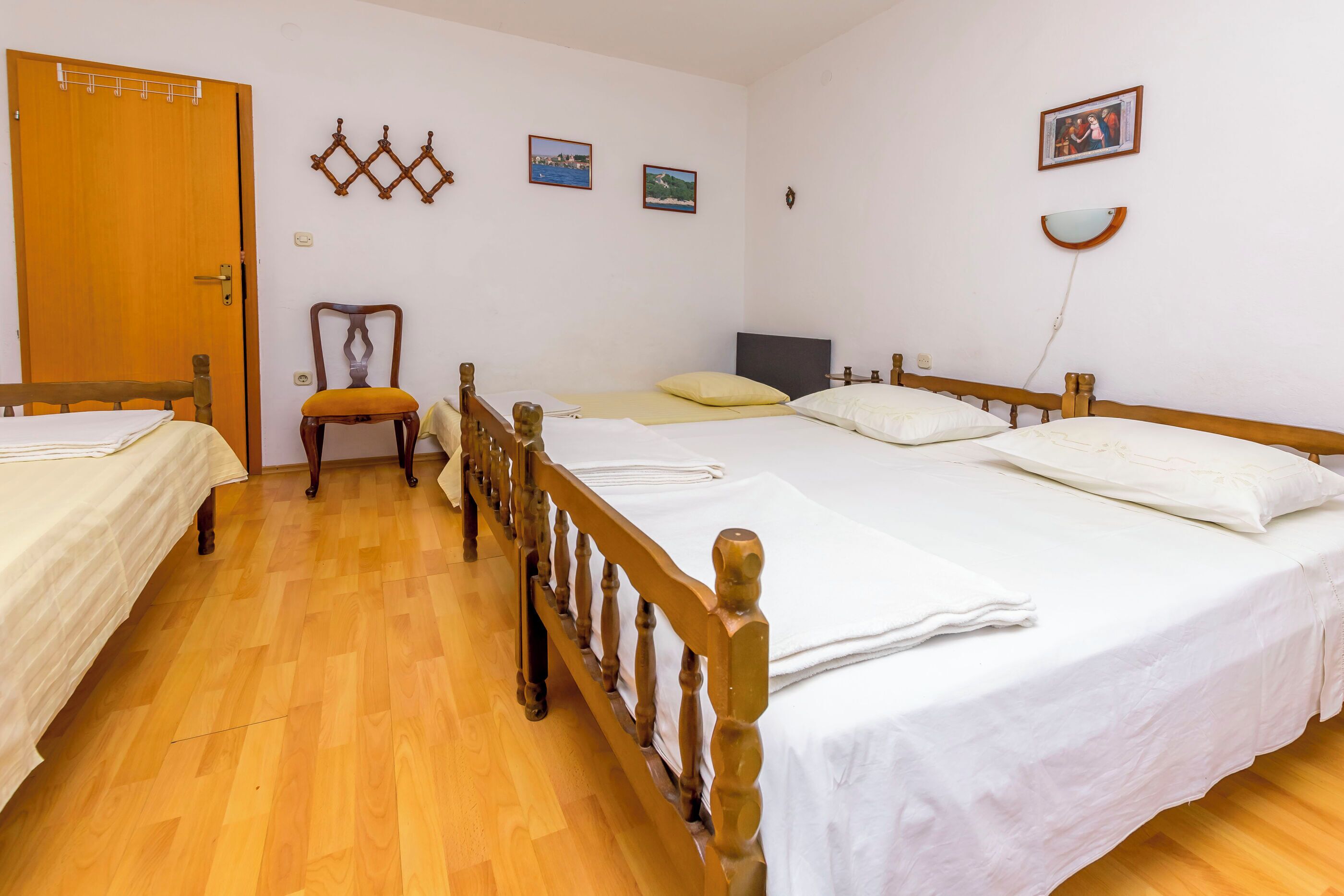 A hotel room with two single beds, a wooden floor, a wooden chair, and a door.