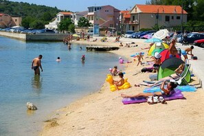 A beach with people swimming and sunbathing, tents, and parked cars.