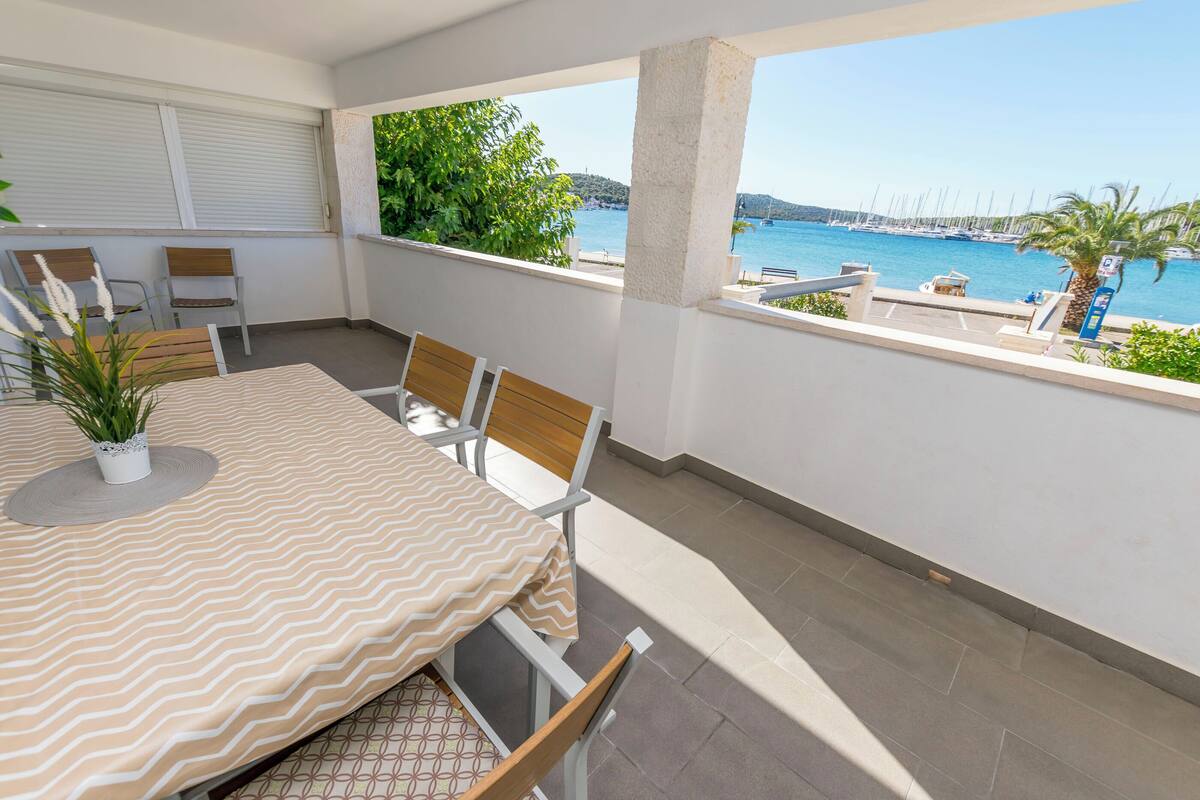 Ein Balkon mit Tisch und Stühlen, mit Blick auf einen Hafen voller Boote und freier Sicht auf das Meer.