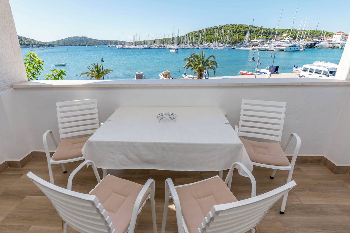Ein Balkon mit Tisch und Stühlen mit Blick auf einen Yachthafen, Boote und eine hügelige Landschaft.