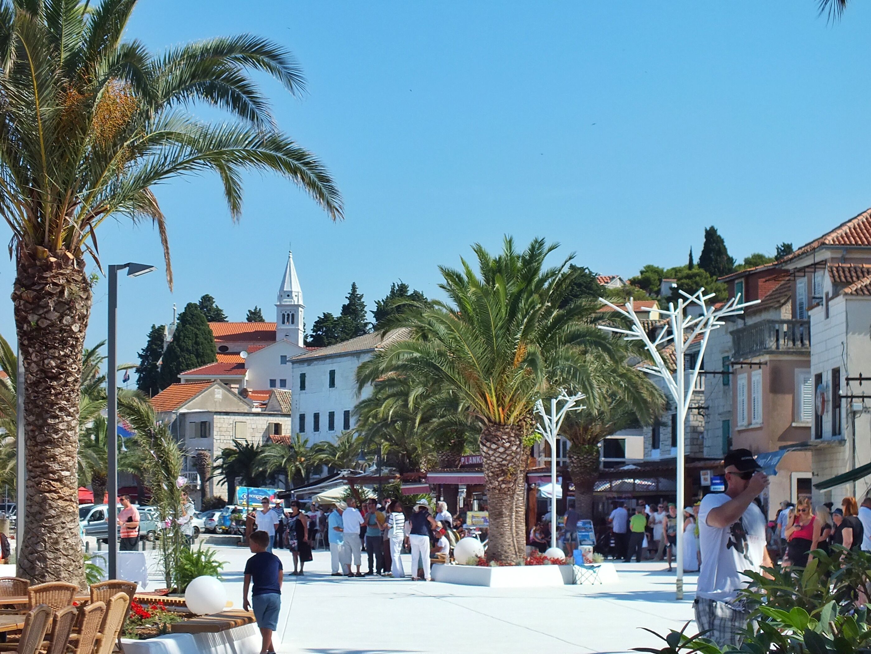 A public square with palm trees, a church, and buildings with traditional architecture.