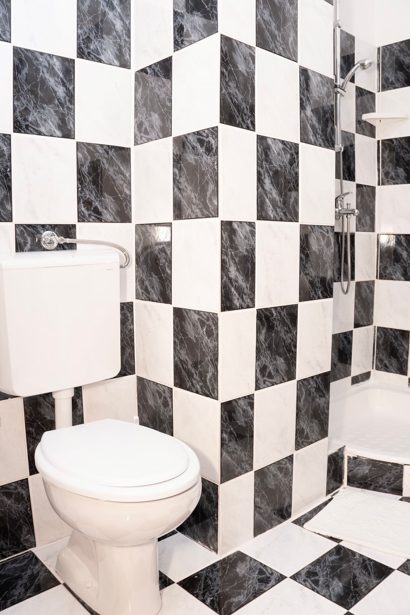 Un baño con inodoro, lavamanos y ducha. Las paredes están cubiertas de baldosas a cuadros en blanco y negro.