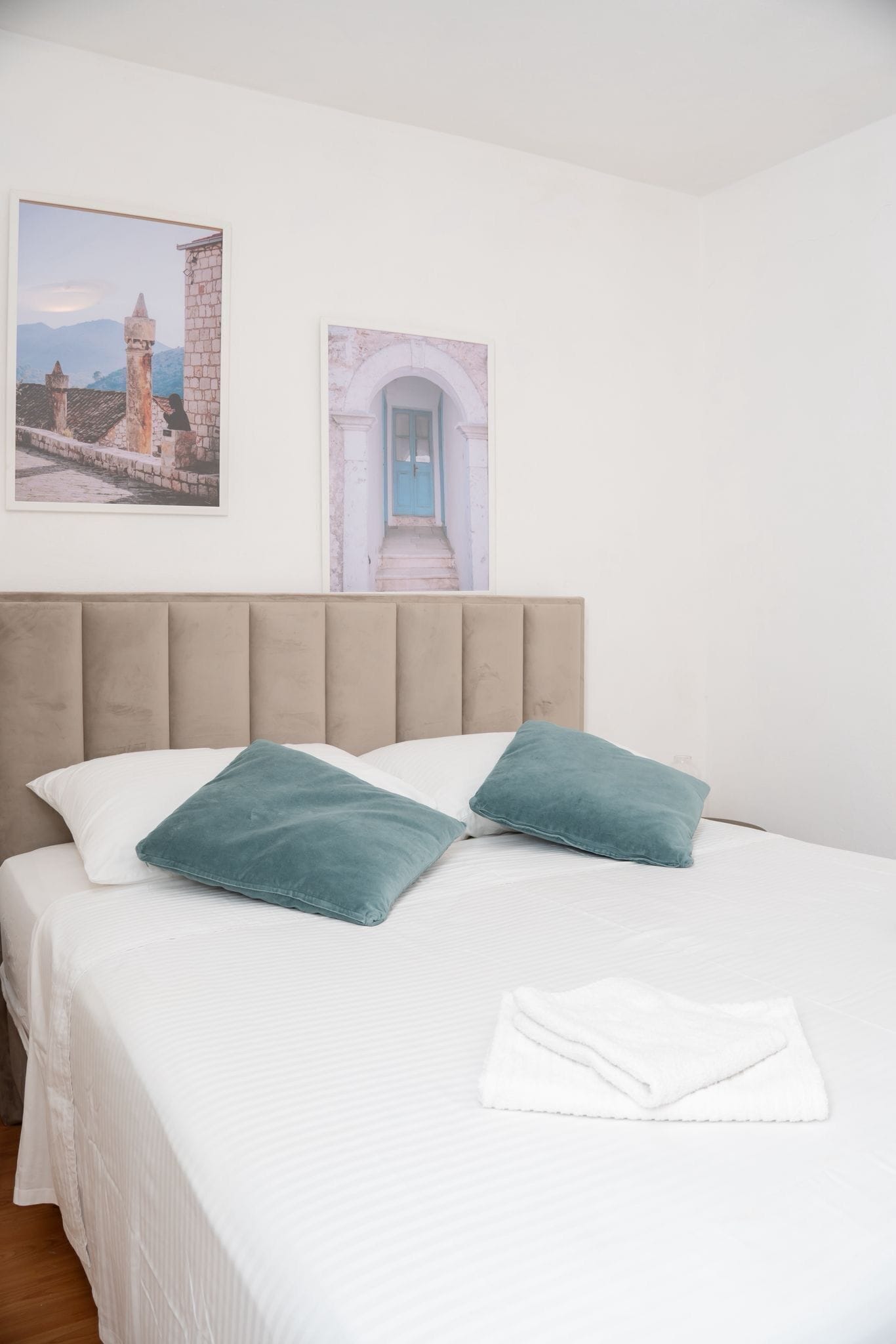 A neatly made bed with two pillows, a folded towel, and two framed pictures on the wall.