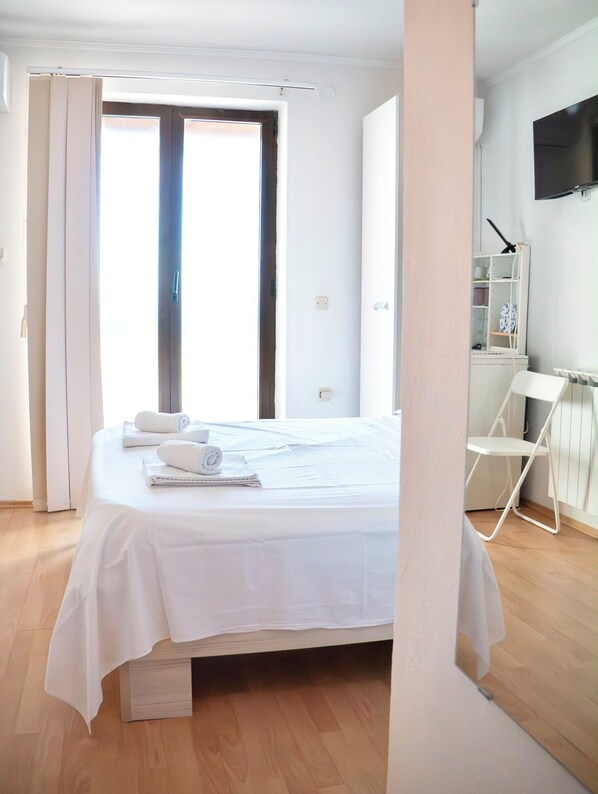 Une chambre à coucher avec un lit, une chaise, un téléviseur et une fenêtre.