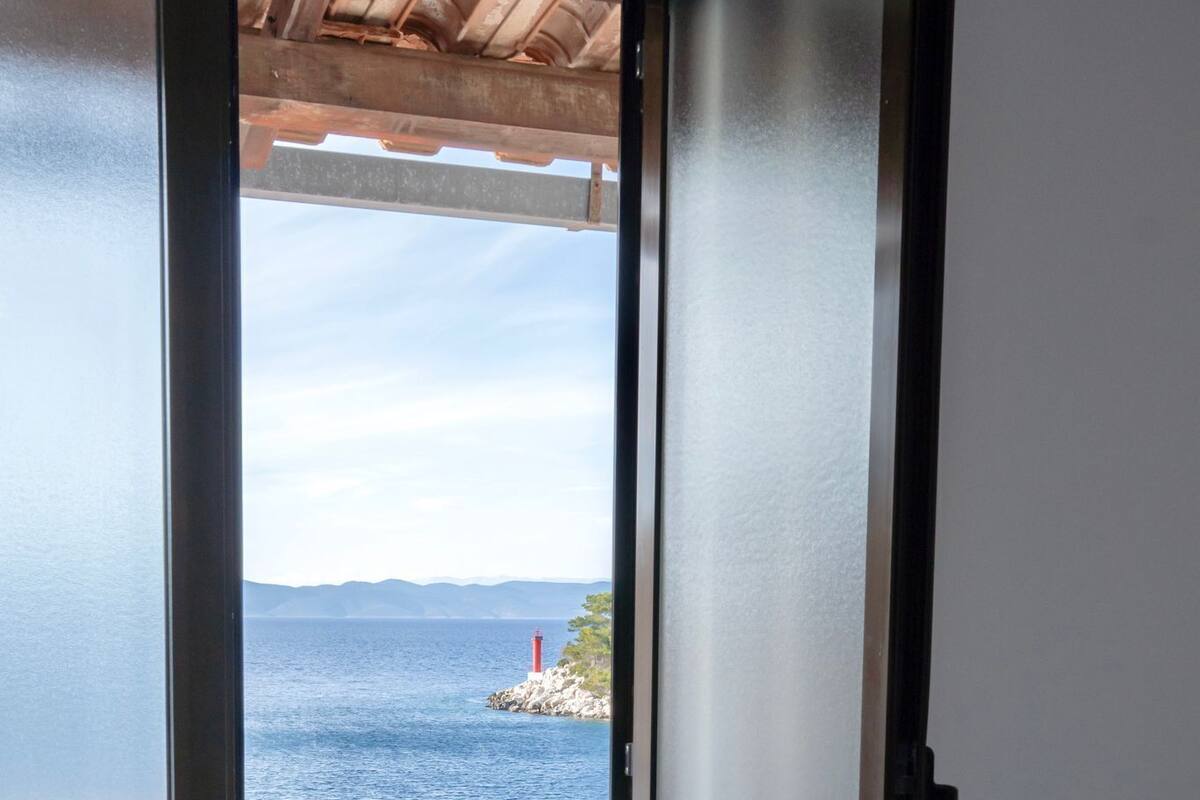 A hotel room with a bed, a white towel, and a view of the sea through an open door.
