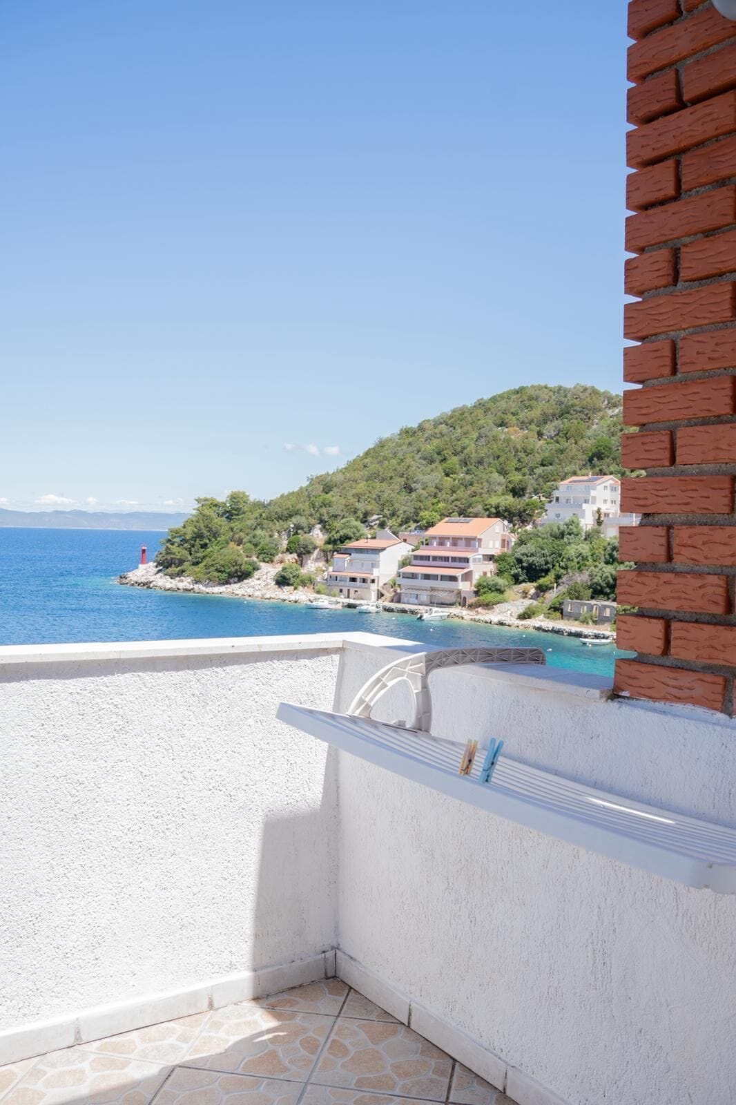 A balcony with a view of a coastal town, a red lighthouse, and buildings on a hillside.