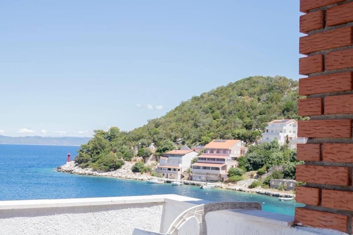 A balcony with a view of a coastal town, a red lighthouse, and buildings on a hillside.