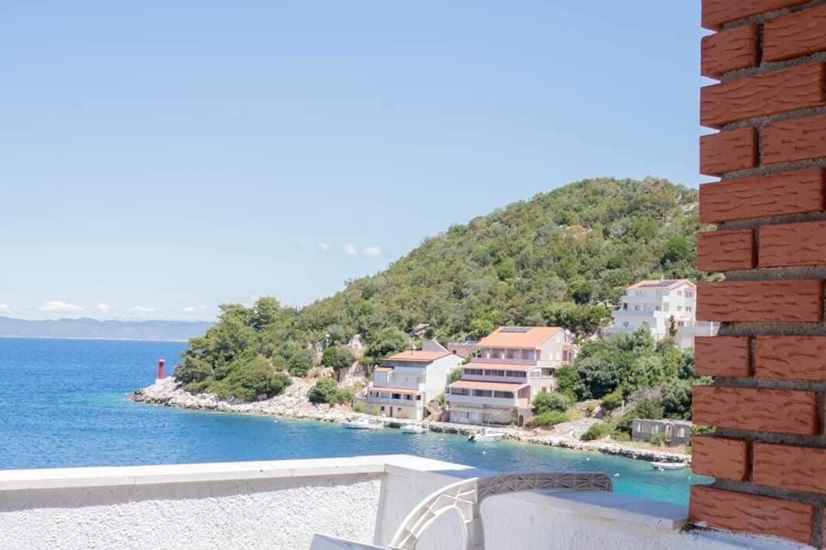 A balcony with a view of a coastal town, a red lighthouse, and buildings on a hillside.