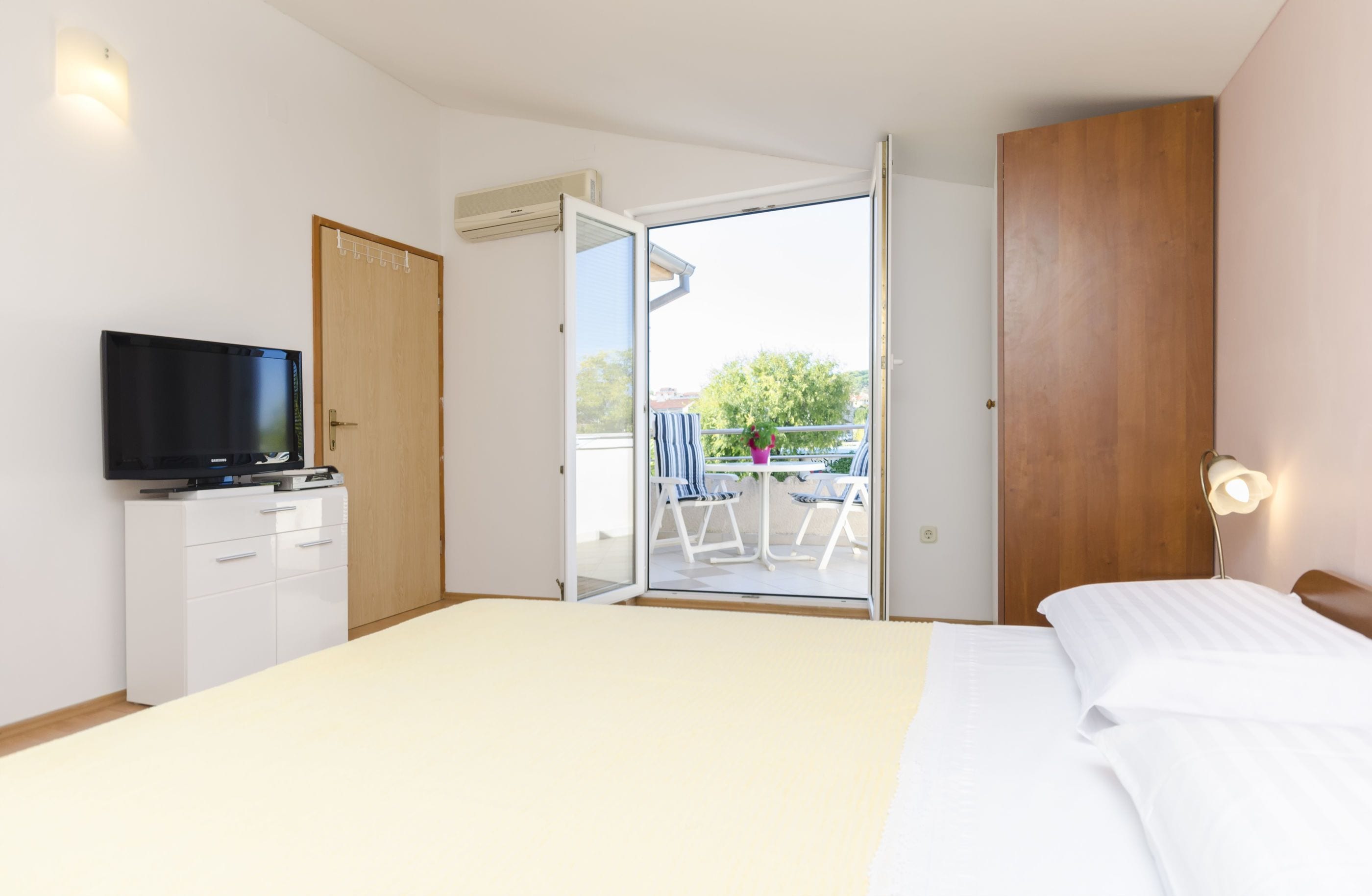 Ein Hotelzimmer mit Bett, Fernseher, Kleiderschrank und einem Balkon mit Stühlen und Tisch.