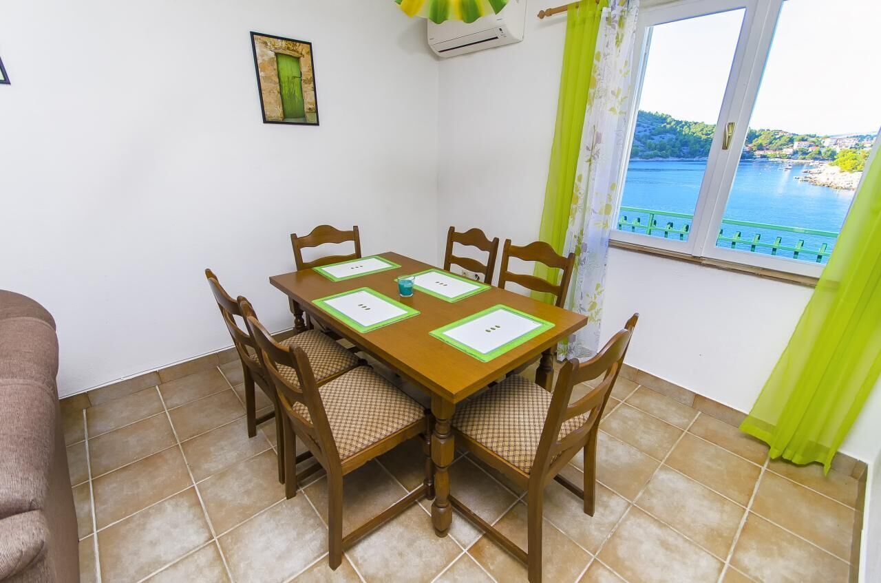 Un coin repas avec une table et des chaises en bois, un tableau encadré au mur et une fenêtre donnant sur un plan d’eau.